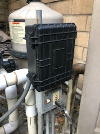 a black box is attached to a pipe in a backyard